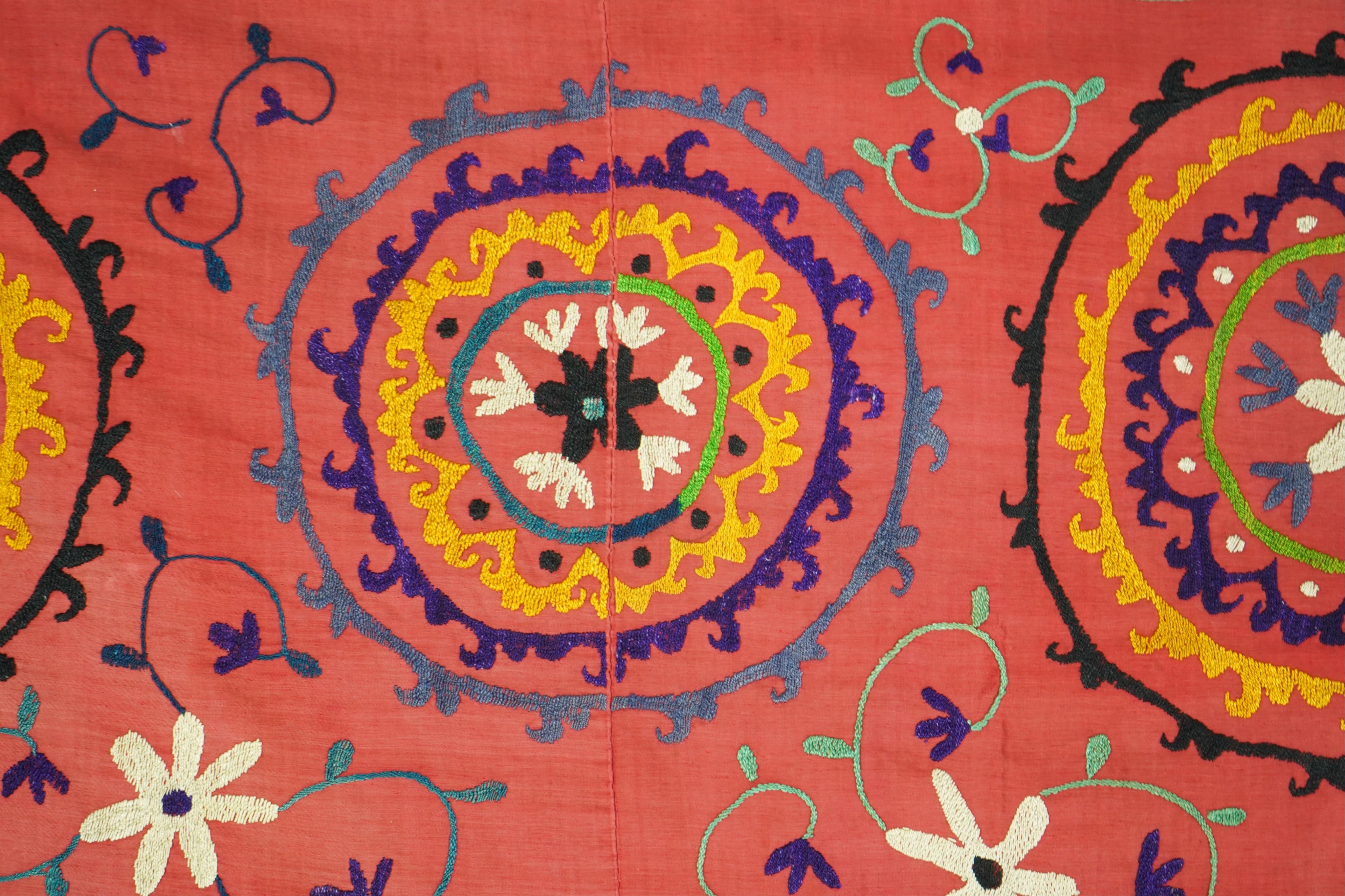 A large 20th century Uzbek multi coloured and embroidered Suzani wall hanging. The word Suzani meaning needlepoint in Farsi. Made in three panels embroidered on a rich dark red background, using large stylised multi colo